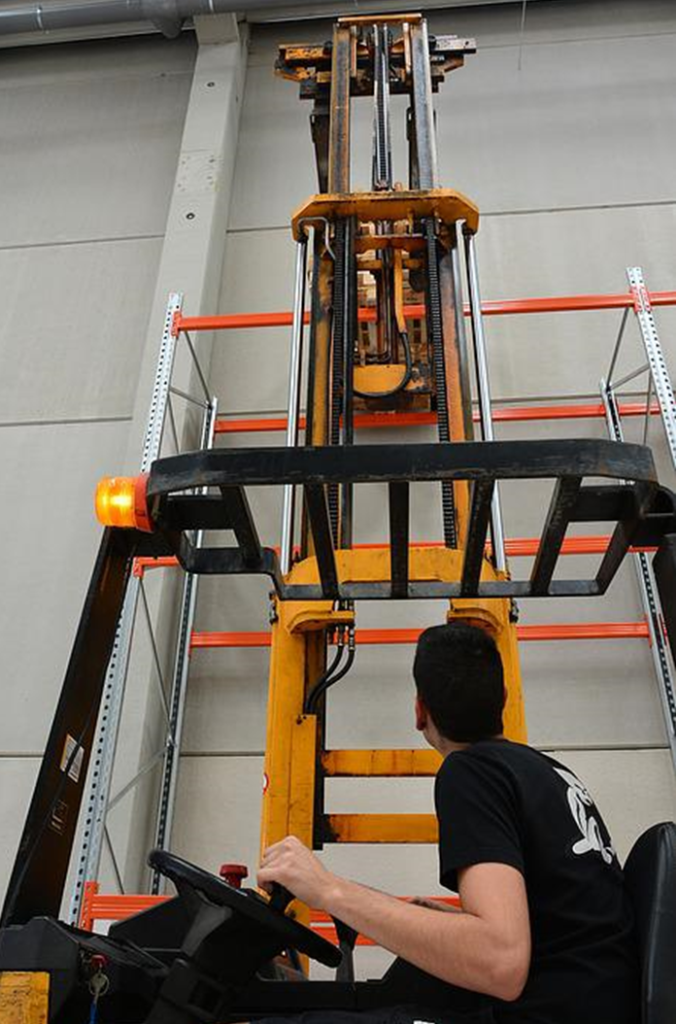 The picture of a reach truck with its higher lifting mast extended. Reach trucks are smaller than forklifts and have a different balance enabling higher lifting mass and the ability to work in tight spaces.