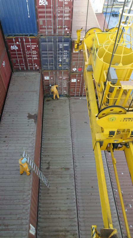 A photo of containers being offloaded from a vessel with personnel wearing protection helmets